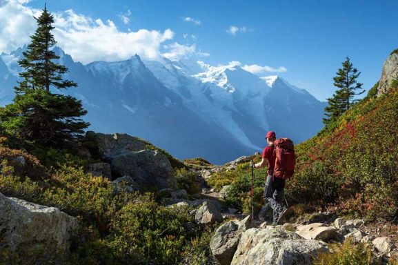 Homme avec un sac à dos marchant dans un paysage montagneux avec des sommets enneigés.