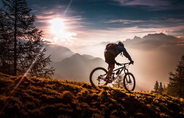 Cycliste sur un sentier montagneux au coucher du soleil, entouré de paysages majestueux.