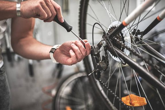 Réparation de vélo avec un outil à main sur la chaîne et le dérailleur.