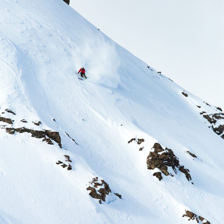 Ski freeride sur une pente enneigée avec de la poudreuse s'élevant autour.