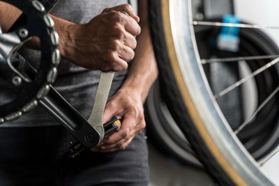 Main dans un atelier, utilisant une clé pour ajuster une pièce de vélo.