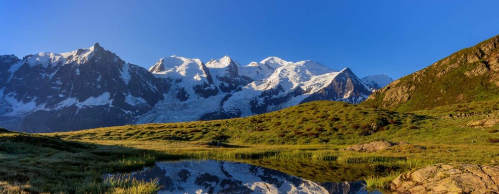 Montagnes enneigées reflétées dans un lac au lever du soleil, avec un ciel bleu.