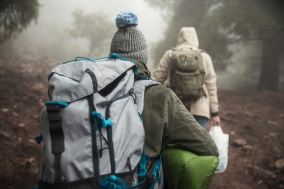 Deux randonneurs avec des sacs à dos marchent dans un environnement brumeux.