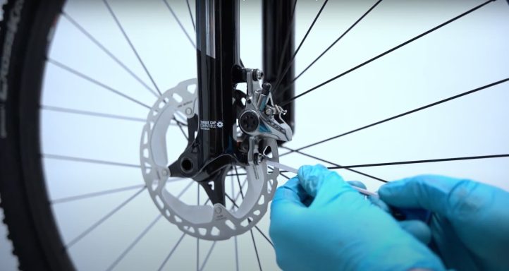 Personne portant des gants bleus ajustant le disque de frein d'une bicyclette.
