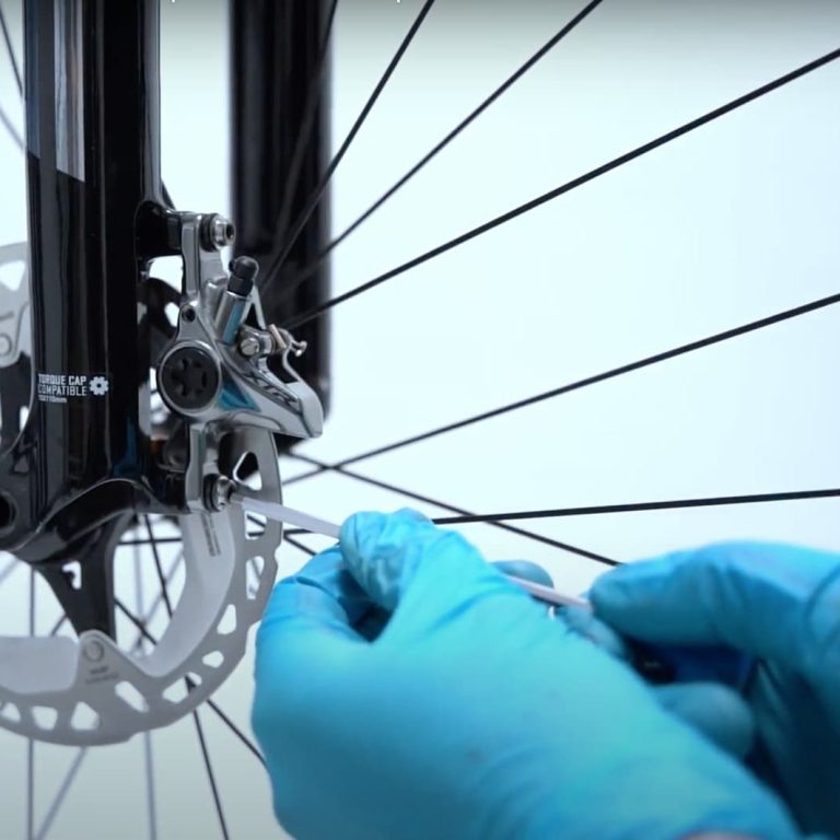 Mains gantées effectuant un réglage sur le frein d'un vélo.